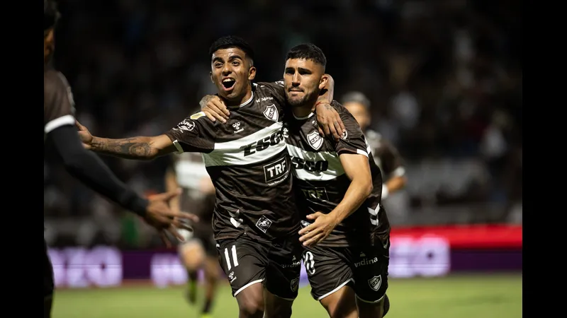 Cầu thủ của Platense đang nỗ lực vượt qua phòng ngự của Deportivo Riestra trong trận đấu.